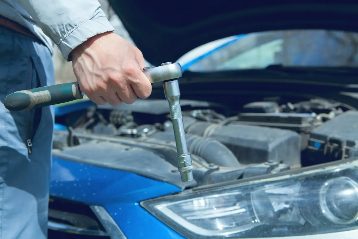 Mão usando uma chave de catraca no motor de um carro