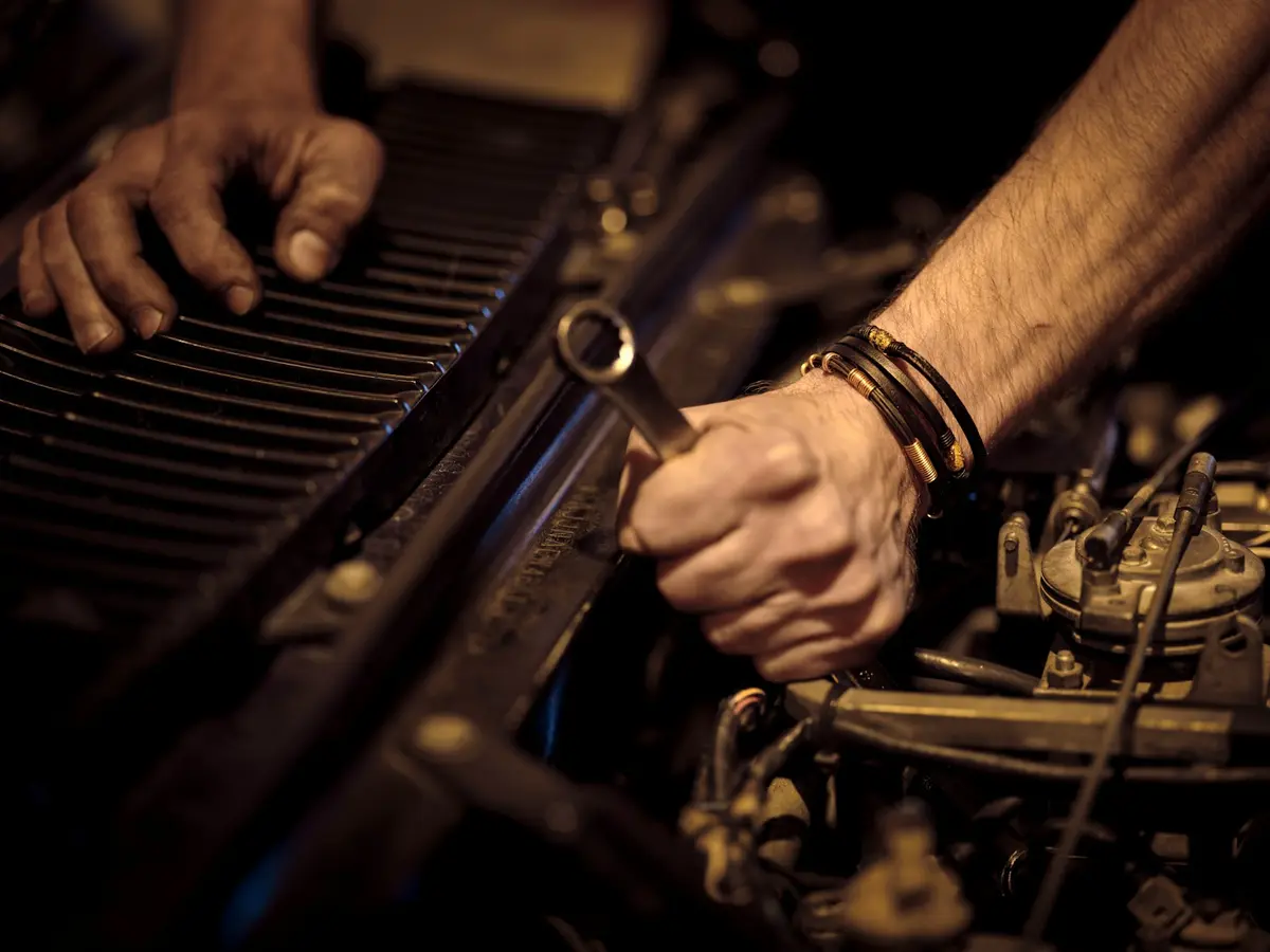 Mãos de mecânico apertando uma peça do motor com uma chave